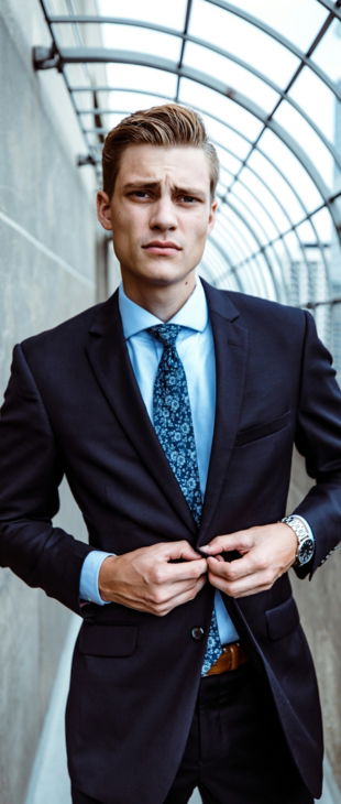 man wearing black and teal dress suit standing near gray wall